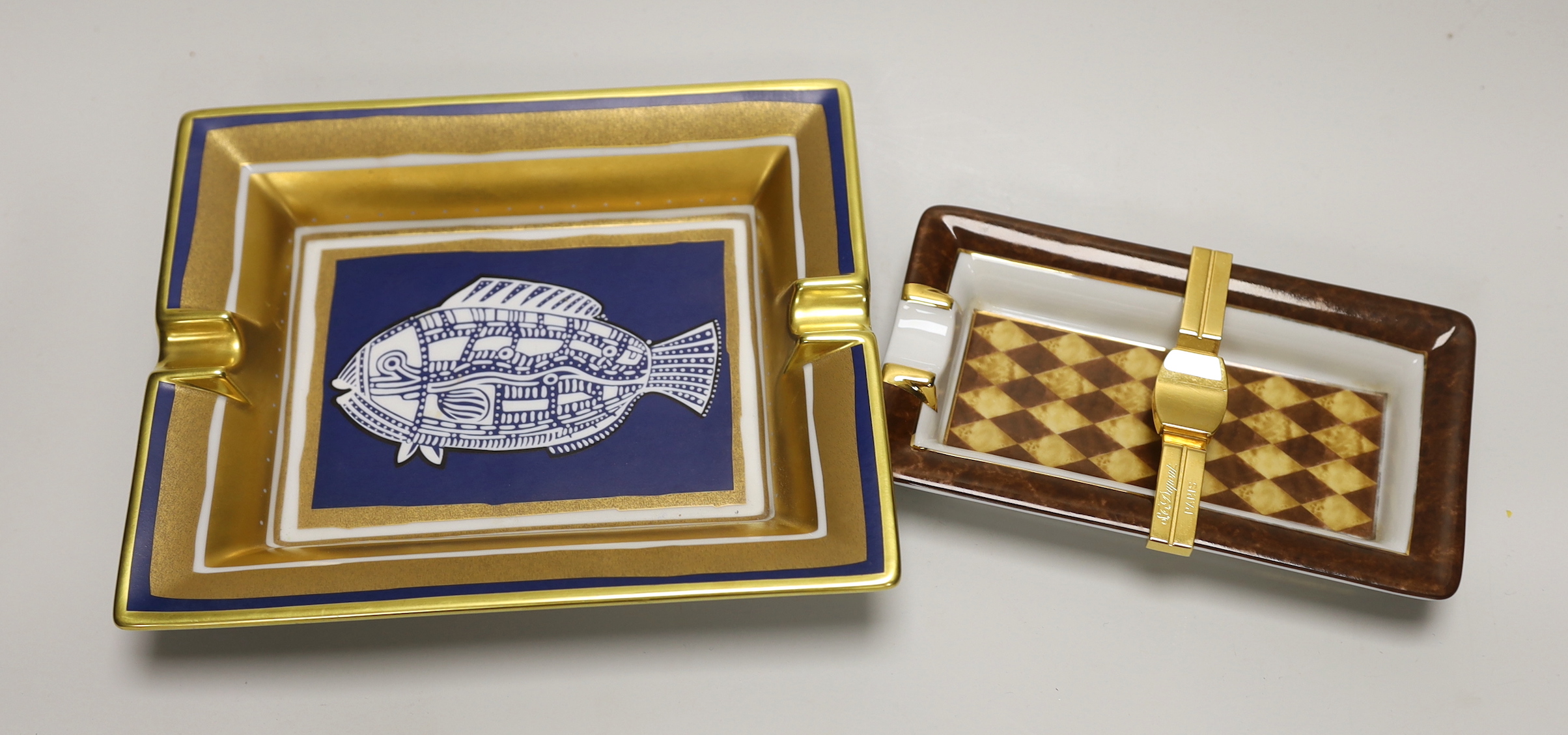 A Hermes-Paris porcelain cigar ashtray decorated with a stylised fish and a similar gilt metal mounted example by Limoges for DuPont, the largest 20cm wide